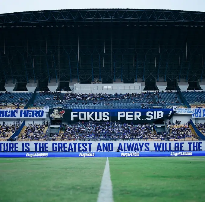 Pemandangan tribun stadion dengan koreografi dan spanduk suporter Persib Bandung saat pertandingan kandang.